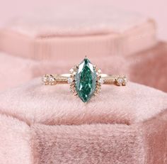 a ring with an oval cut green stone surrounded by small white diamonds on a pink blanket