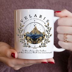 a woman holding a white coffee mug with the words velarris on it and mountains in the background