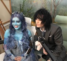 two people dressed in costumes sitting next to each other with makeup on their faces and hair