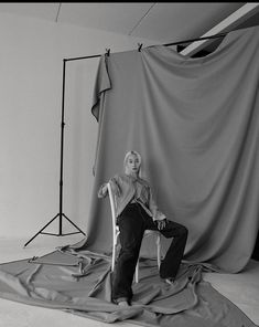 a black and white photo of a woman sitting on a chair in front of a backdrop