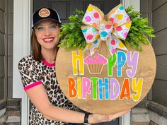 a woman holding up a happy birthday sign in front of a door with a cupcake on it