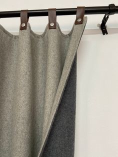 a curtain hanging on a black rod next to a white wall with a brown leather handle