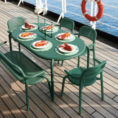 the table is set with plates of food and chairs on the deck overlooking the water