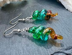 Enhance your accessory collection with these Unique Lampwork Glass Dangle Earrings featuring  hollow dangles in transparent emerald, teal, and topaz. Measuring 2" long, these stylish earrings are sure to make a statement wherever you go. Perfect for the fashion-forward individual who appreciates unique and handcrafted jewelry. Handmade by skilled glass artisan, Alisha White. Embrace the blend of artistic tradition and modern style with these handcrafted treasures, and let your earrings be a conv Earrings Handmade Dangle, Stylish Earrings, Leaf Coloring, Stylish Earring, Glass Artists, Glass Earrings, Custom Boxes, Jewelry Handmade, Earrings Handmade