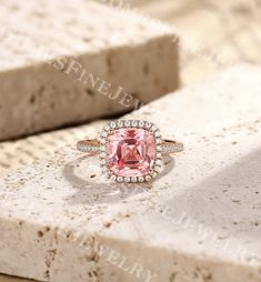 an engagement ring with a large pink stone surrounded by diamonds on top of a rock