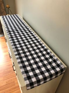 a black and white checkered tablecloth is on the edge of a wooden dresser