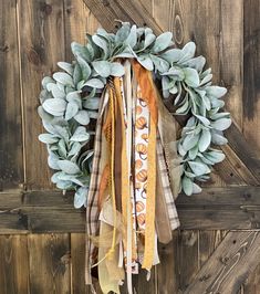 a wreath hanging on the side of a wooden door with leaves and ribbons around it