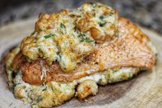 a piece of meat covered in cheese and sauce on top of a wooden plate with other food items