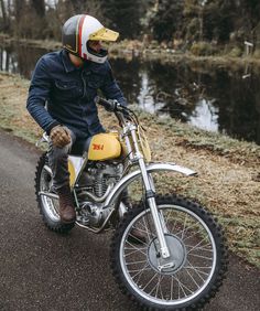 a man riding on the back of a dirt bike down a road next to a river