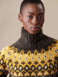 a woman with short hair wearing a yellow and black knitted turtle - neck sweater