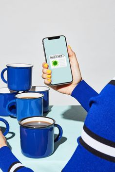 a woman is holding up her phone while sitting at a table with coffee cups and mugs