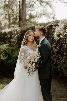 a bride and groom standing together in front of bushes