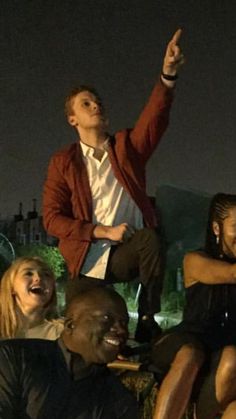 a group of people sitting on top of each other in front of a building at night