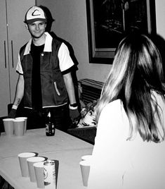 black and white photograph of two people standing at a table with cups in front of them