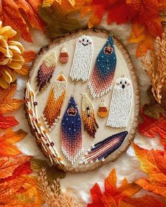 beaded halloween decorations are displayed on a tree slice surrounded by autumn leaves and flowers