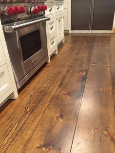 a wood floor in a kitchen with white cabinets and stainless steel stove top ovens