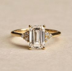 an emerald cut engagement ring with three diamonds on the band and side stones in yellow gold