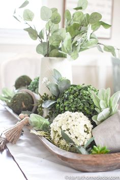 a table topped with vases filled with flowers and greenery on top of a wooden tray