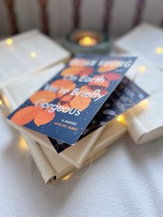 three books are stacked on top of each other in front of a candle and some candles