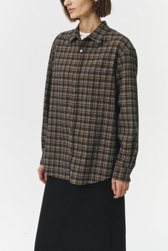 a woman wearing a black and brown checkered shirt with long sleeves, standing against a white background