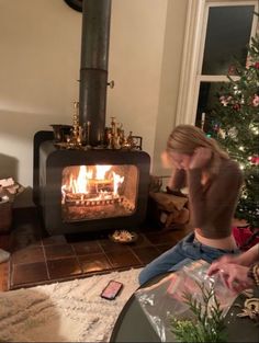 a man sitting in front of a fire place next to a christmas tree and phone