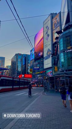 a person riding a bike down a street next to tall buildings with billboards on them