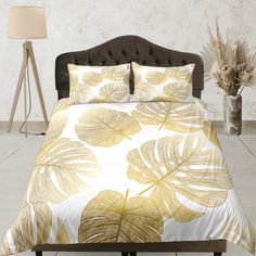 a bed with a white and yellow comforter on top of it next to a lamp