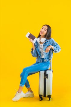 a young woman sitting on top of a suitcase holding a book and listening to headphones