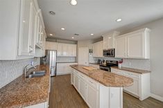 a large kitchen with white cabinets and granite counter tops, along with an island in the middle