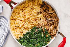 a pan filled with pasta, spinach and mushrooms