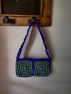 a crocheted purse hanging on a wall with a chalkboard in the background