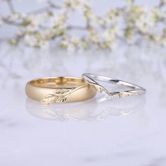 two gold wedding rings sitting next to each other on top of a white table with flowers in the background