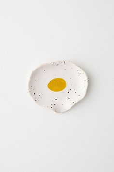 an egg on a white plate with black speckles in the shape of a fried egg