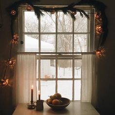 a bowl of fruit sitting on top of a table next to a window covered in christmas lights