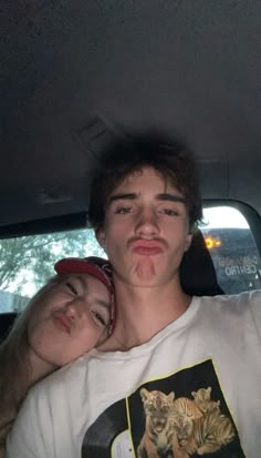 a young man and woman sitting in the back seat of a car with their tongue out