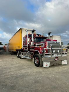 a red and yellow semi truck parked in a parking lot with other trucks behind it