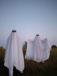 two people in white cloths standing in tall grass with their heads covered by covers