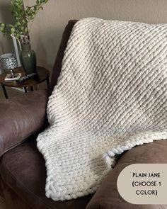 a white blanket sitting on top of a brown couch next to a potted plant