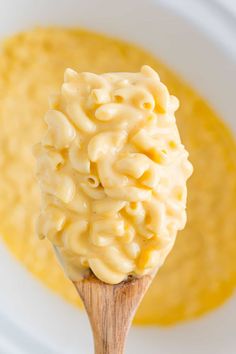 a wooden spoon filled with macaroni and cheese soup on top of a white plate