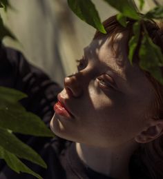 a woman with red hair is looking up at leaves