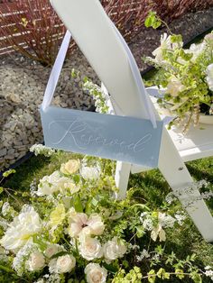 a white chair sitting in the grass with flowers on it and a sign that says reserved