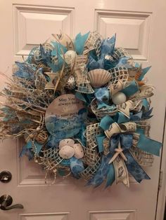 a wreath is hanging on the door with blue and white ribbons, seashells and pearls