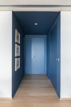 an empty hallway with blue walls and pictures on the wall in front of it's doors