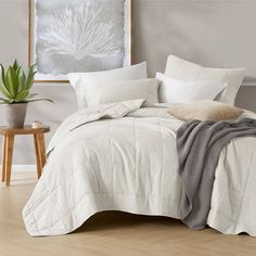 a bed with white sheets and pillows in a room next to a potted plant