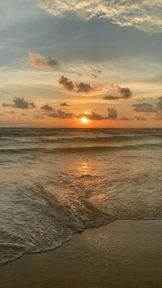 the sun is setting over the ocean with waves coming in to shore and some clouds