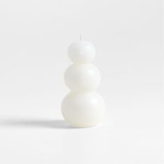 a white candle sitting on top of a table next to a white wall and floor