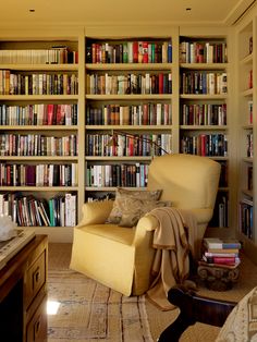 a living room filled with lots of books on top of a book shelf next to a chair