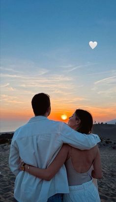 a man and woman standing on top of a beach under a heart shaped balloon in the sky