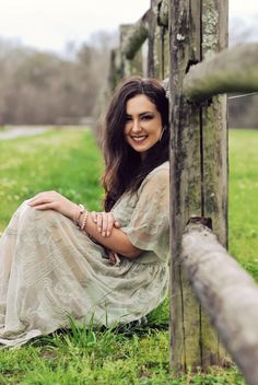 a woman sitting on the ground next to a wooden fence in a green field with grass