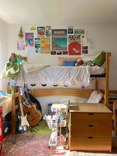 a bedroom with a bed, desk and guitars on the wall next to each other